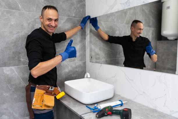 A bathroom remodeler in a black shirt and gloves stands in front of a sink, preparing for renovation work.